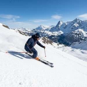 Skier carving down a snowy mountain slope under blue sky