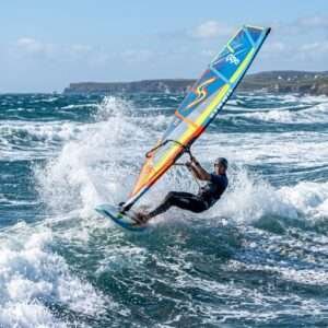 A windsurfer speeding through ocean waves with a colorful sail